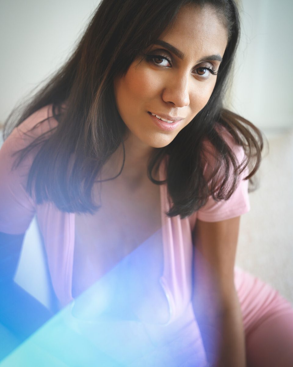 Woman in a pink top seated by a window, a blue and violet prism flare sweeping across the lower frame
